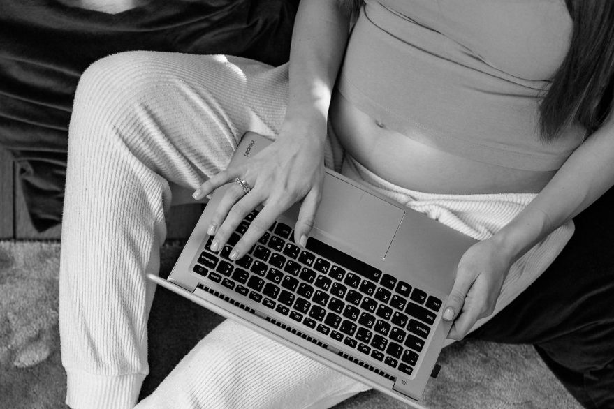 Eine schwangere Frau sitzt an einem Laptop.