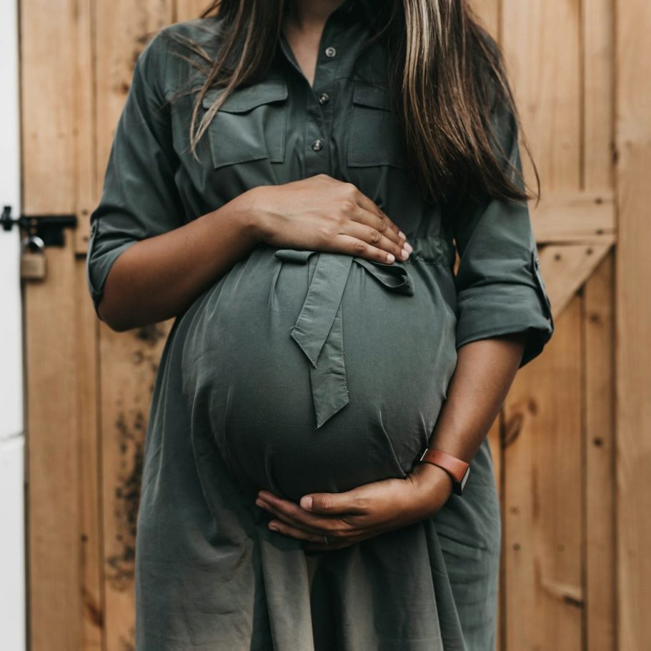 Schwangere Frau umfasst mit beiden Händen ihren Babybauch.