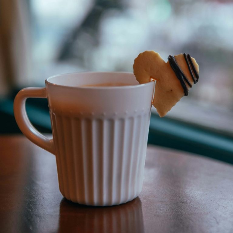 Foto von Fatemeh Rz auf Unsplash Eine Tasse Kaffee steht auf einem Tisch mit einem Keks in Herzform am Rand der Tasse.